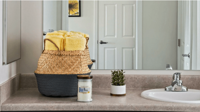 A neatly organized bathroom countertop with a basket of yellow towels, soap, and a small plant.