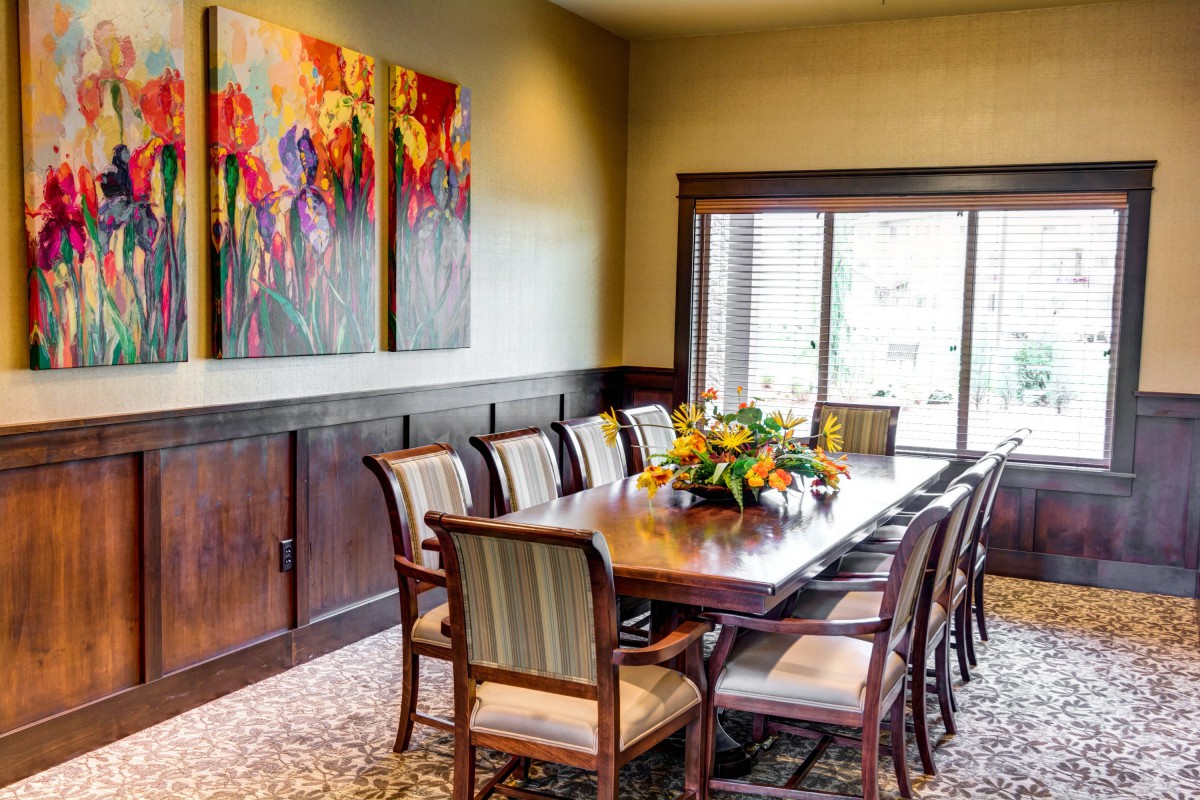 A bright dining room with a large table and chairs, decorated with colorful artwork and a floral centerpiece.