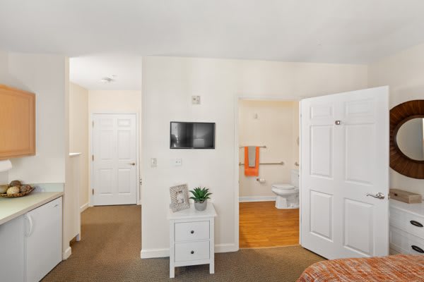 A cozy bedroom interior with an adjacent bathroom, featuring white walls and simple decor.