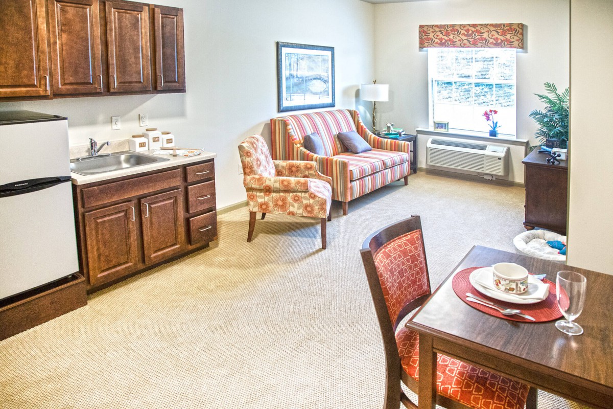 A cozy living area with a kitchenette, sofa, table, and large window.