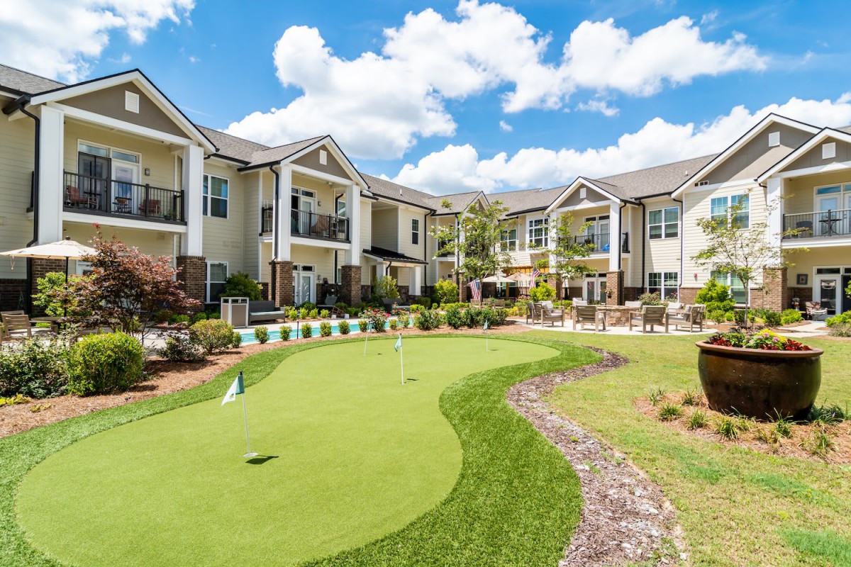 A modern apartment complex with a well-maintained golf putting green in the courtyard on a sunny day.
