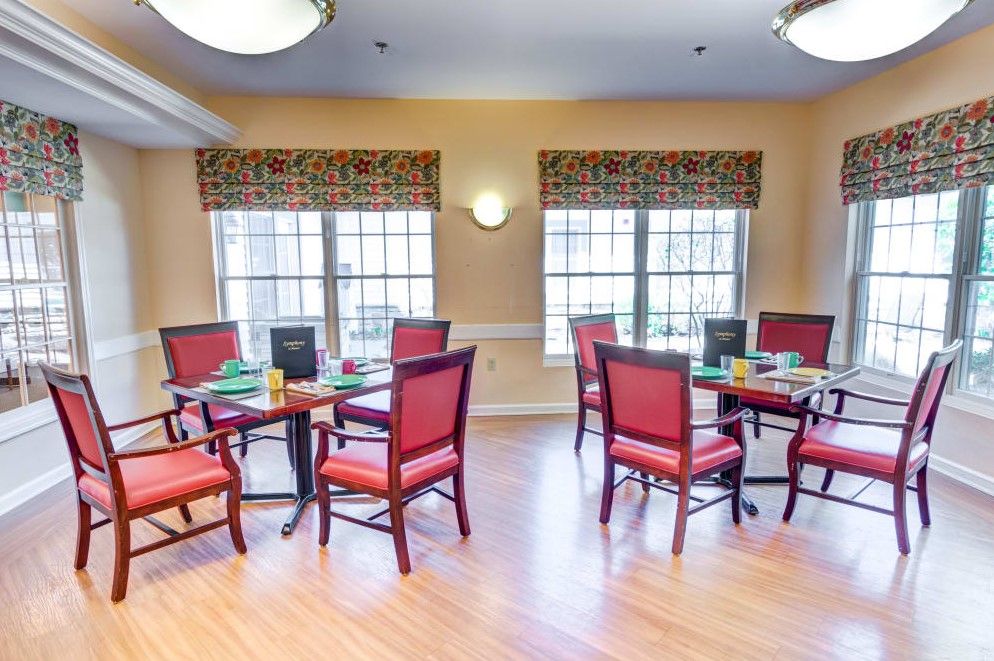 A cozy dining area with several tables and chairs, lit by natural light from large windows.