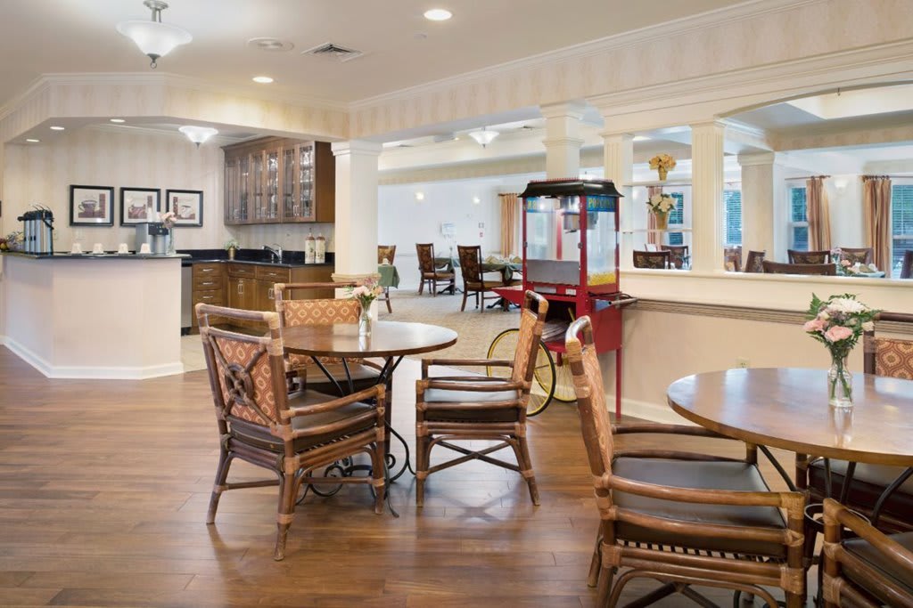 A cozy seating area with wooden tables and chairs, featuring a popcorn machine and kitchen in the background.