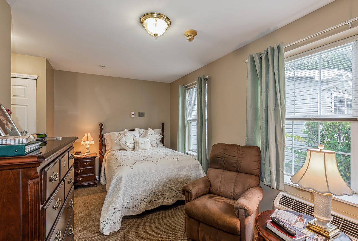 A cozy bedroom featuring a double bed, armchair, and dresser with soft lighting and curtains.