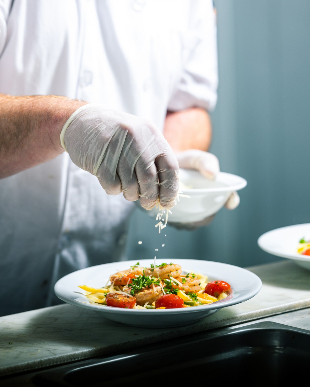 A chef garnishing a pasta dish with herbs in a restaurant kitchen.