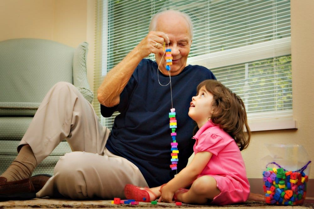 A grandfather and his grandchild happily playing with colorful toys indoors.