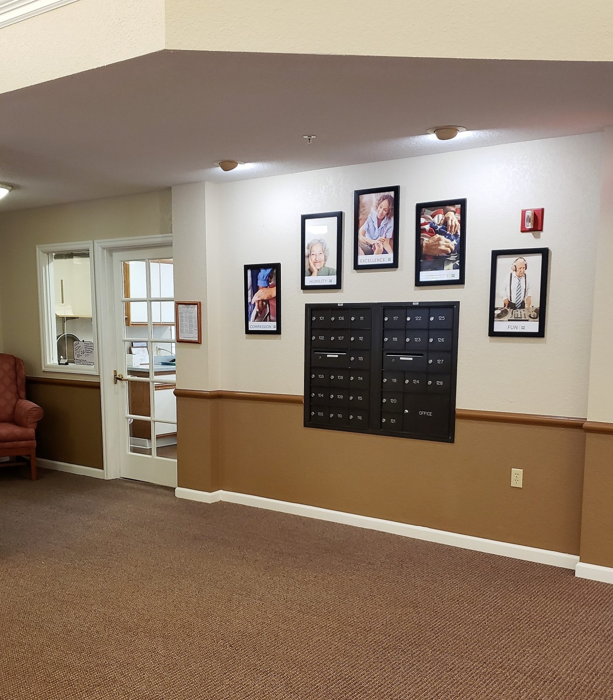 A hallway with mailboxes and framed photos on the wall, featuring carpet flooring and ambient lighting.
