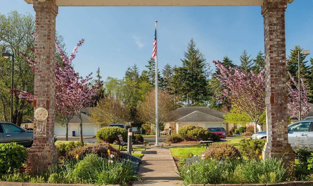 A well-maintained garden with a flagpole, surrounded by blooming trees and houses.