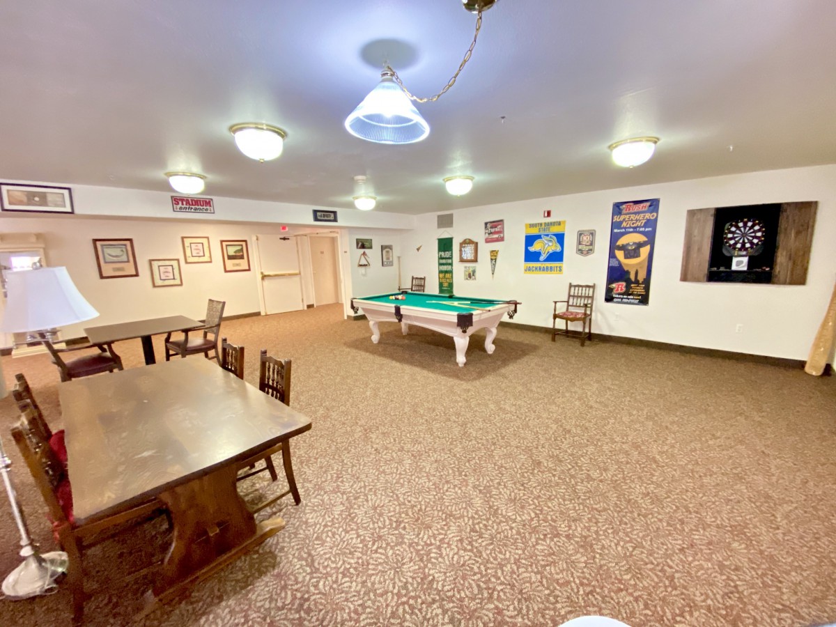 A recreation room with a pool table, tables, and chairs surrounded by posters on the walls.