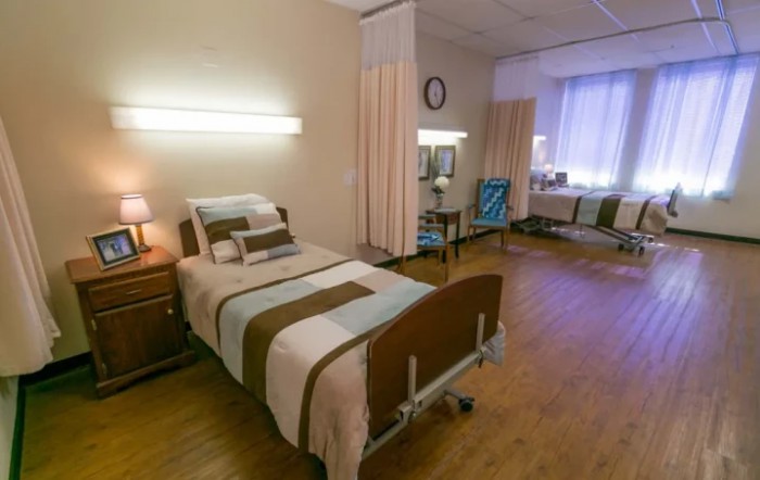 A hospital room with a single bed, bedside table, and curtain dividers.