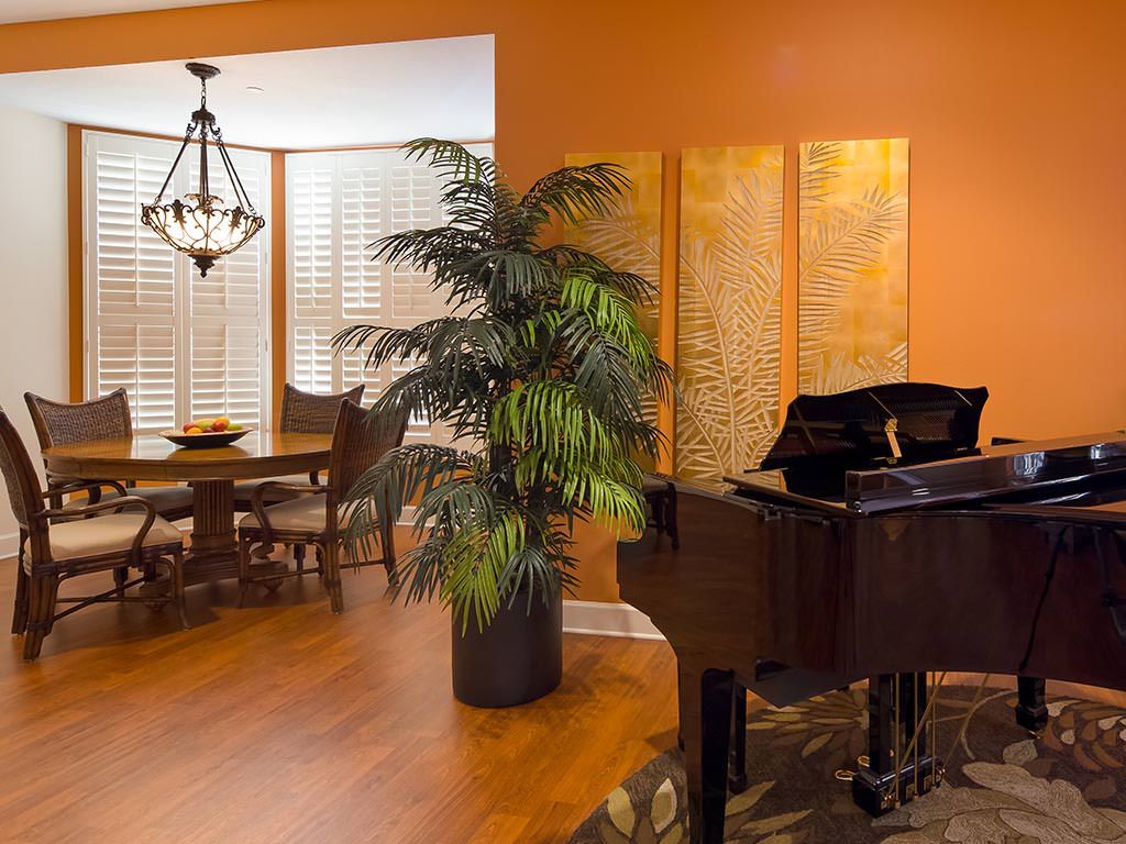 A warm and inviting living room with a grand piano, an indoor plant, and a dining area with elegant decor.