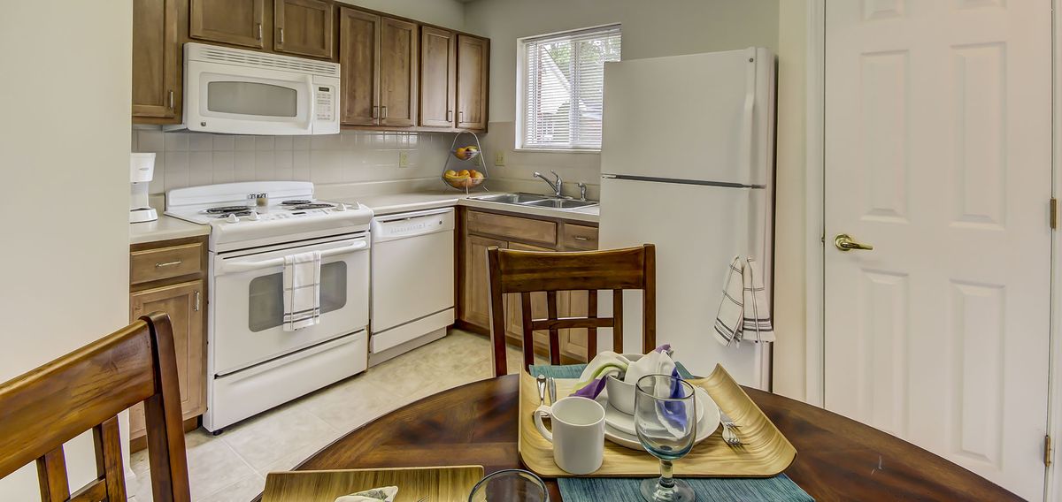 A cozy kitchen with wooden cabinets and white appliances, featuring a small dining table set for a meal.