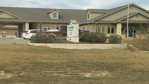 A view of a residential building with a sign and parked vehicles in front.