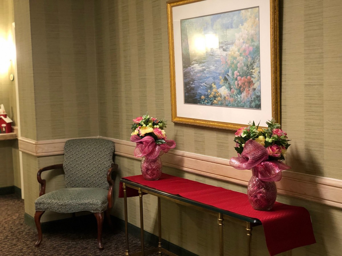 A decorated room corner featuring two floral bouquets on a table beneath a framed painting.