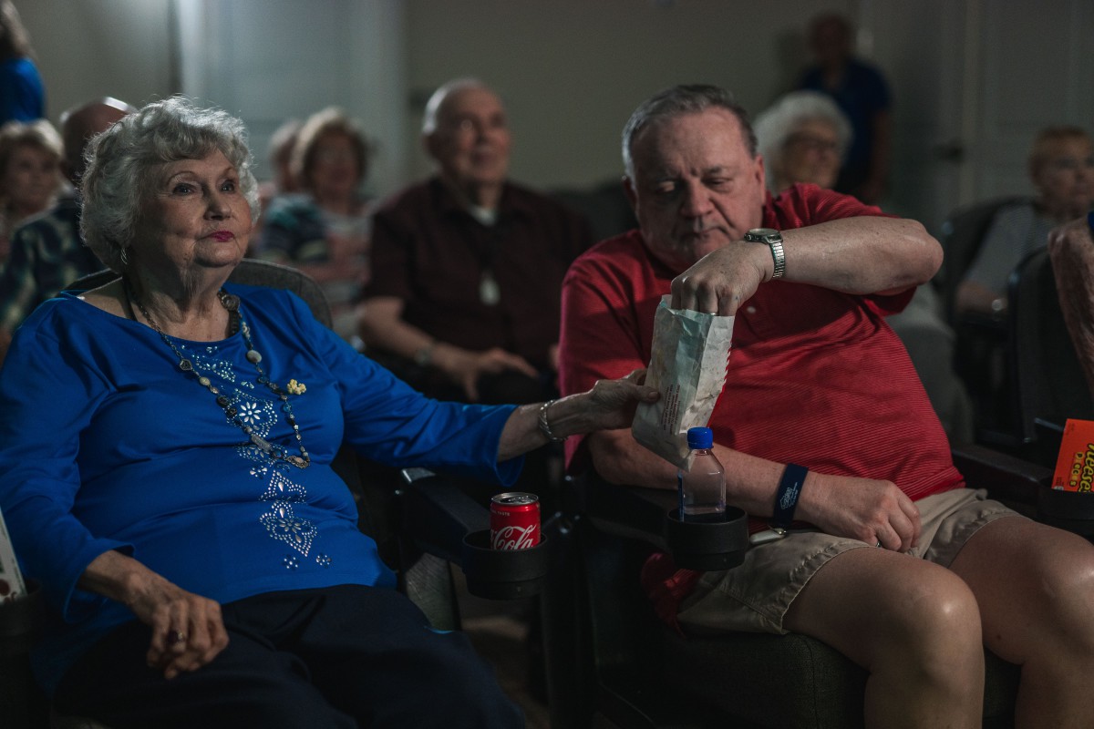 A group of elderly people enjoying a movie night, with one man reaching for popcorn.