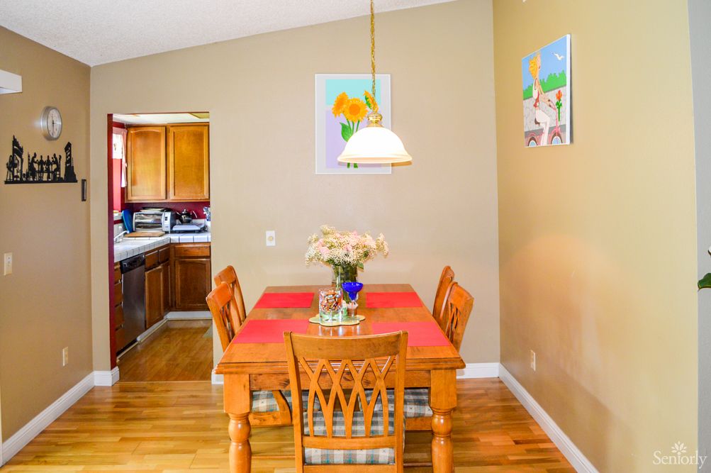 A cozy dining area with a wooden table set for four, featuring a flower vase centerpiece, adjacent to a kitchen.