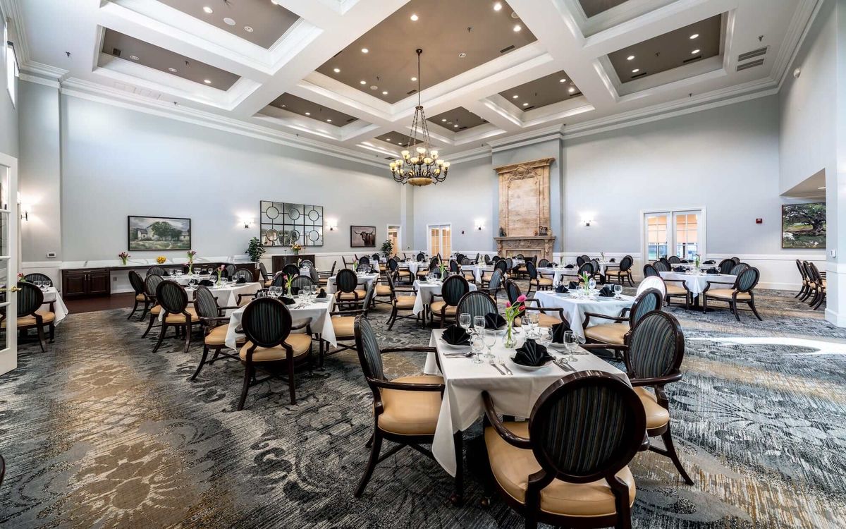 An elegant restaurant dining area with neatly arranged tables and chairs, featuring chandeliers and sophisticated decor.