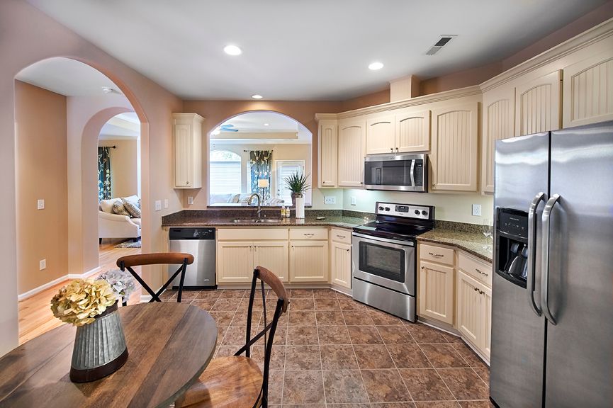 A modern kitchen with wooden cabinets, stainless steel appliances, and a tile floor, featuring an adjacent dining area.