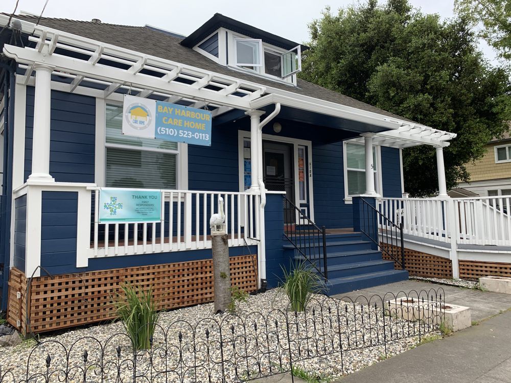 A blue house with a white porch and several business signs, featuring landscaping and decorative fencing.