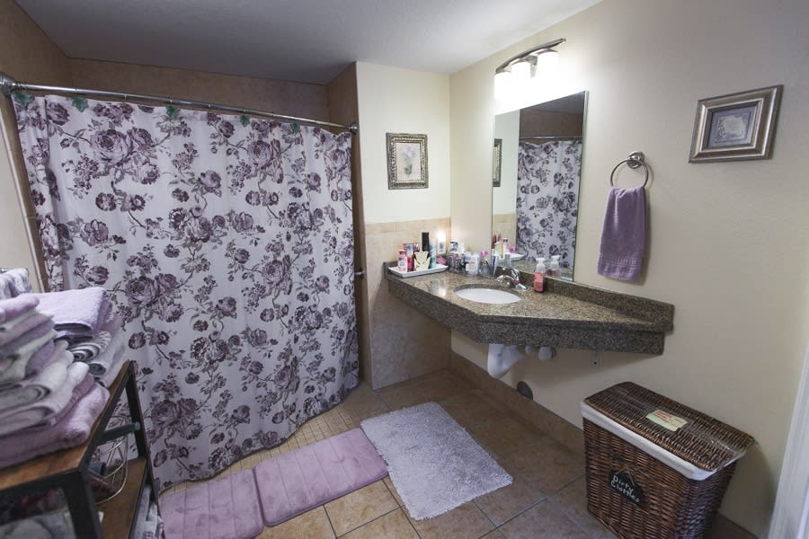 A cozy bathroom featuring a floral shower curtain, a countertop with toiletries, and pastel-colored bath mats and towels.