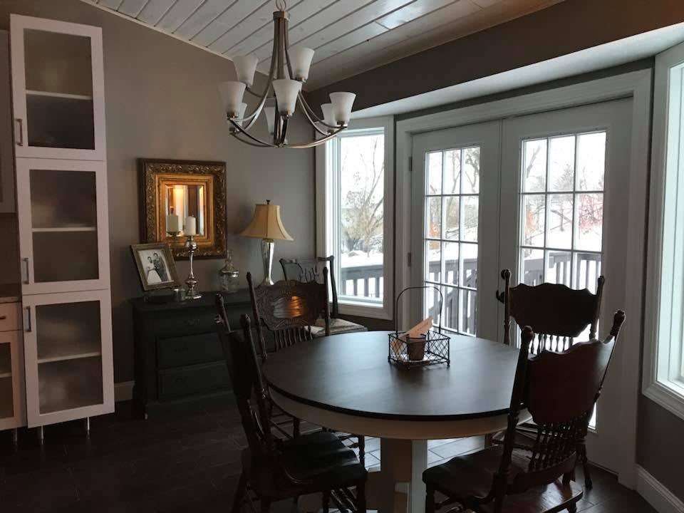A cozy dining room with a round table, chairs, and a chandelier, illuminated by natural light from the French doors.