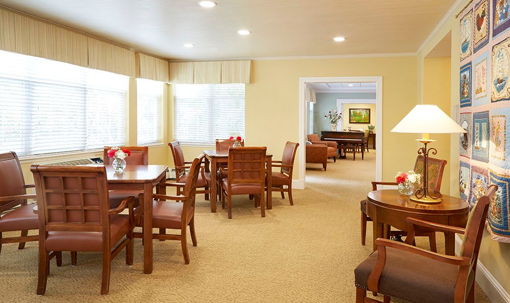 A bright dining area featuring wooden tables and chairs with large windows allowing natural light.