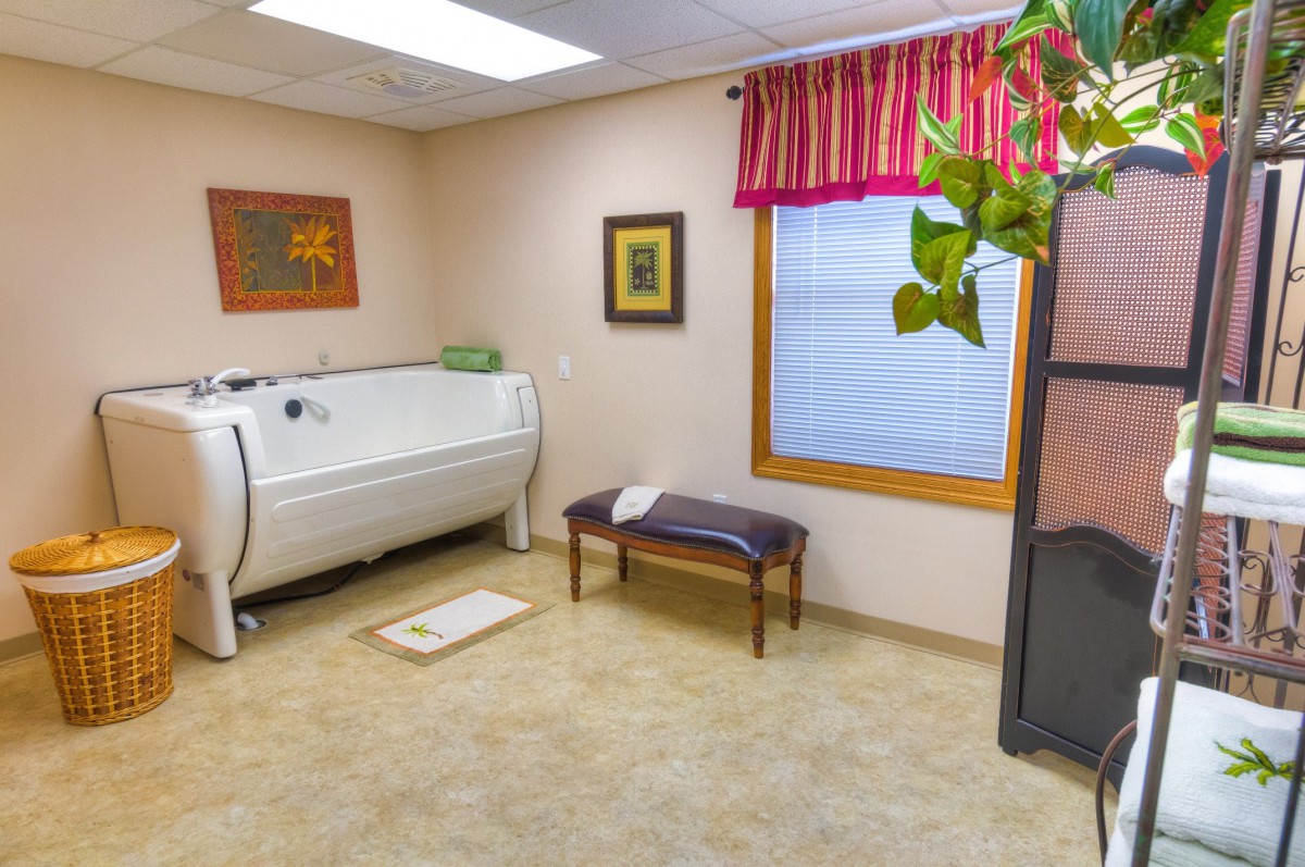 A clean and cozy room with a bathtub, bench, and decorative elements.