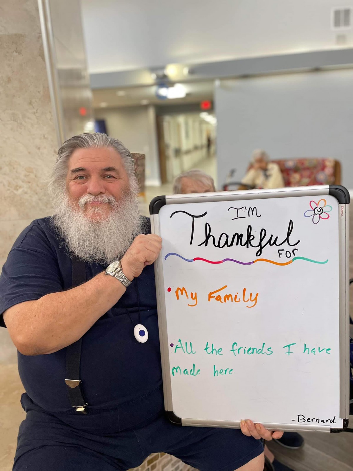 A man with a beard smiles while holding a whiteboard that lists things he is thankful for.