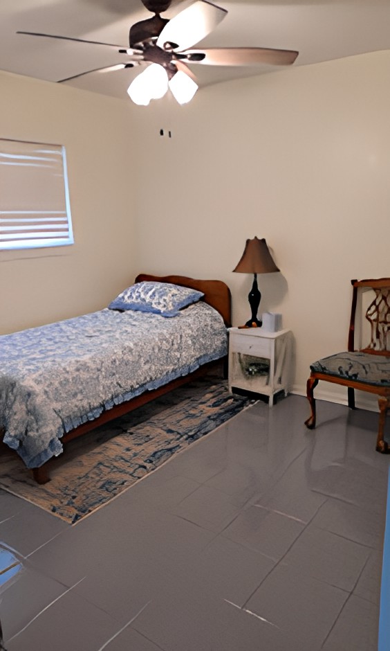 A minimalist bedroom featuring a single bed, nightstand with a lamp, and a chair.