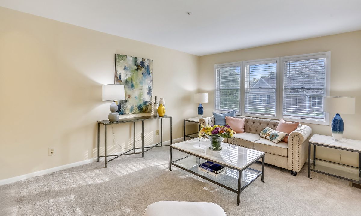 A bright and welcoming living room with modern decor, featuring a comfortable sofa, coffee table, artwork, and large windows.