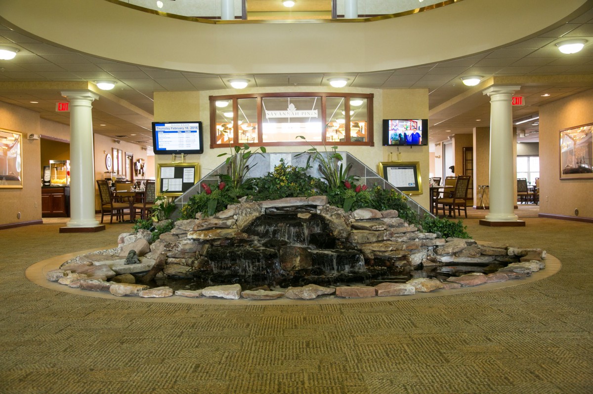 A spacious lobby area featuring a central fountain with surrounding seating and multiple screens.