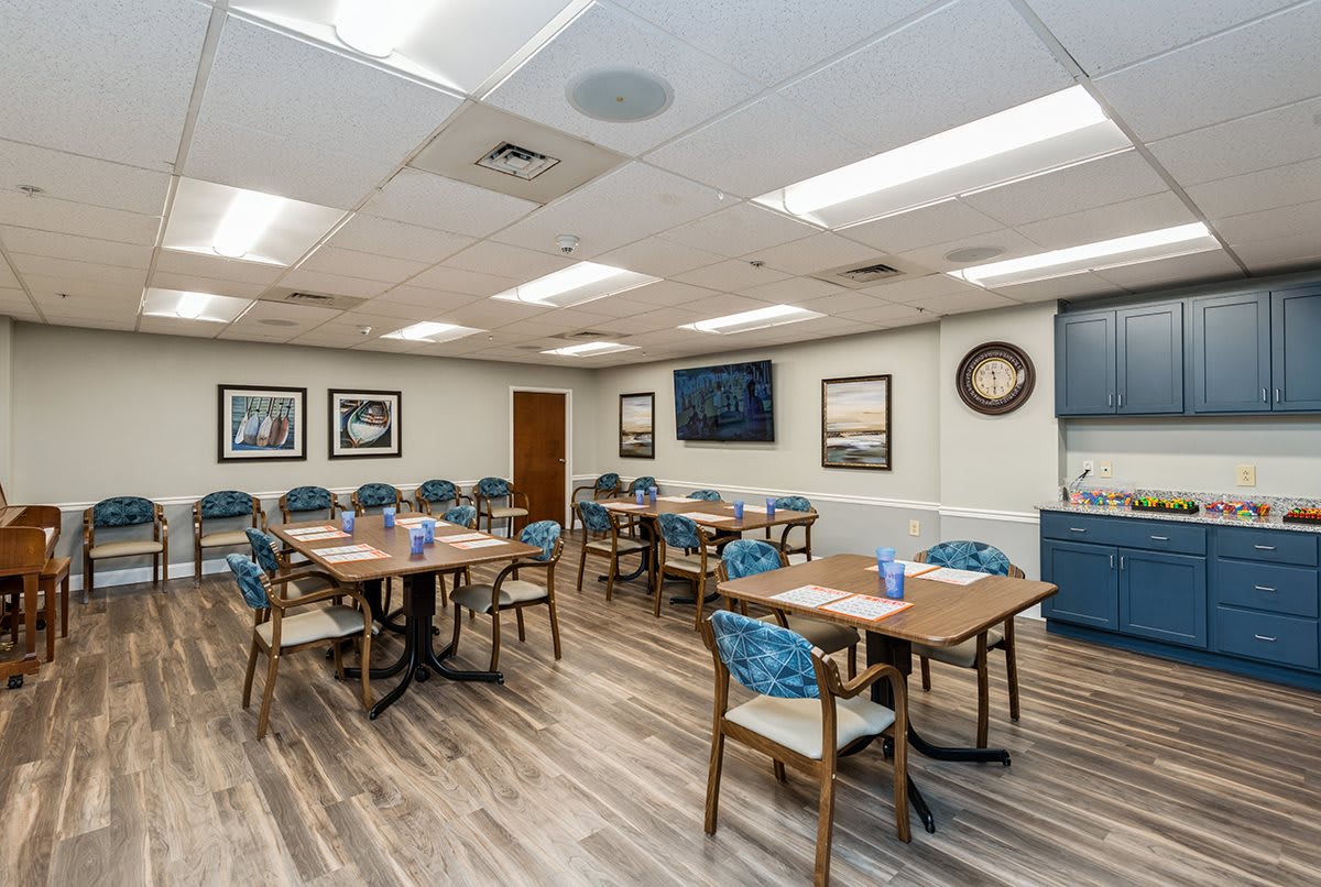A well-lit meeting room with several tables and chairs, featuring a large television and wall art.