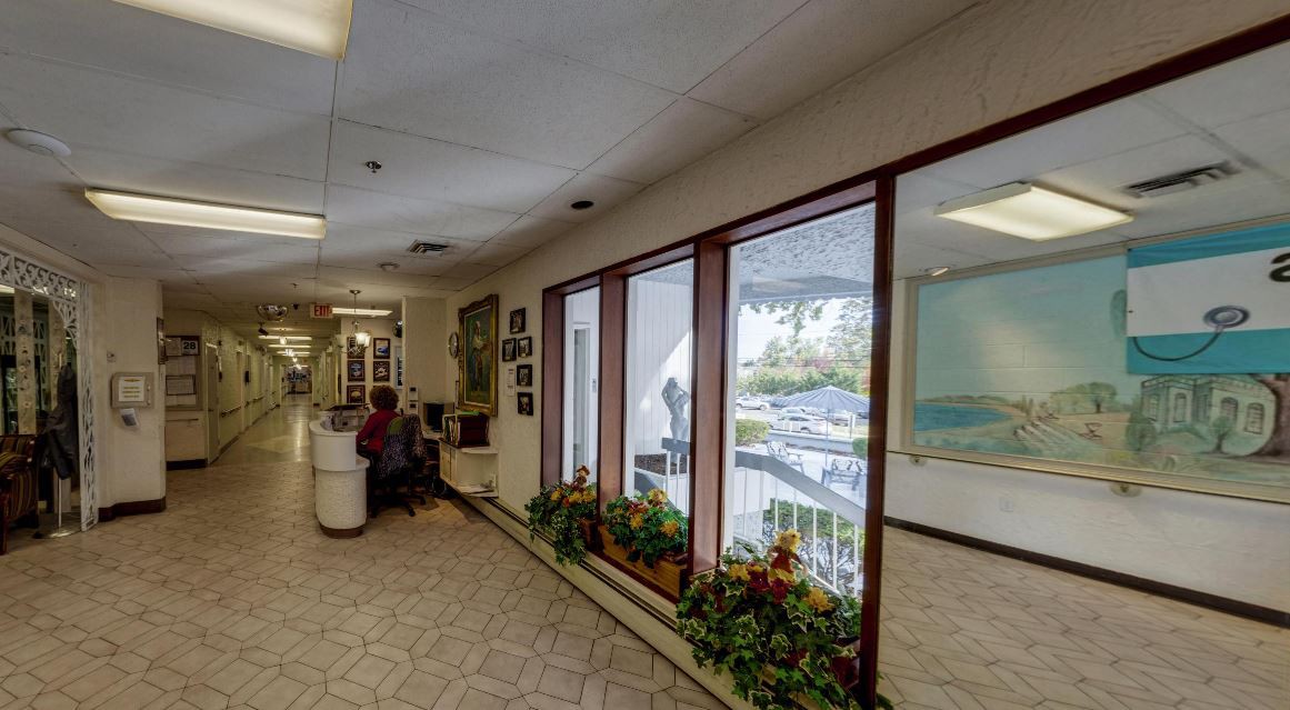 A spacious office waiting area with a reception desk, large windows, and indoor plants.