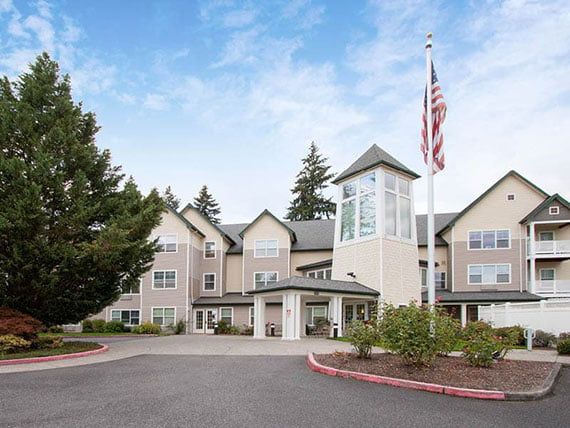 A residential building with a flagpole and surrounding trees under a blue sky.