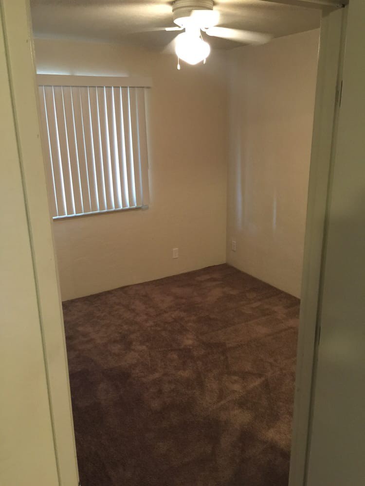 An empty room with carpeted flooring and a window with vertical blinds.