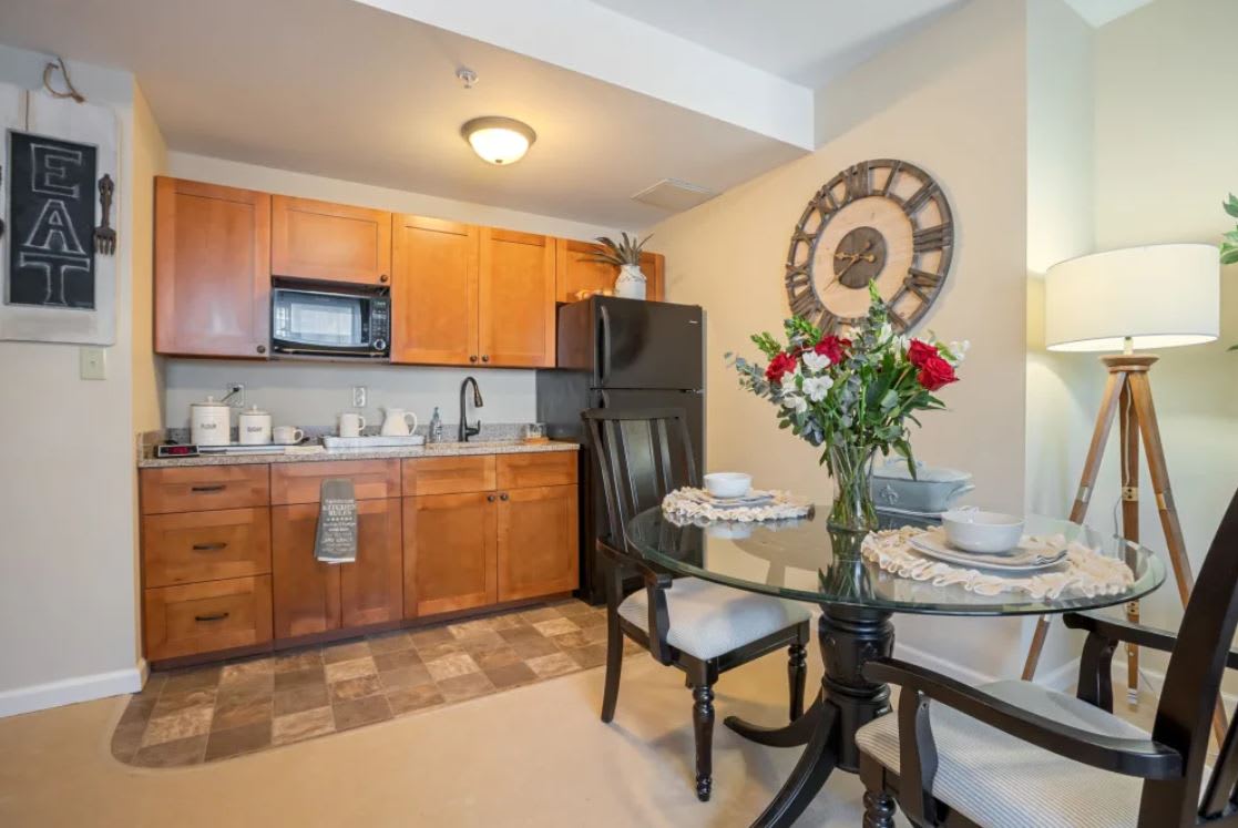 A cozy kitchen with wood cabinetry and a small dining table, adorned with red and white flowers.