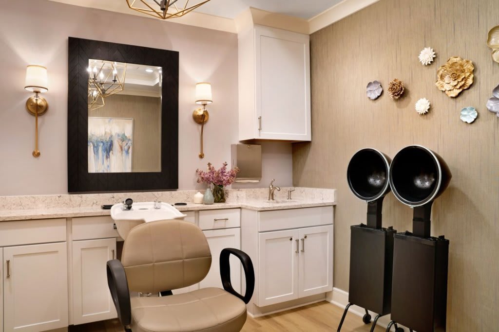 A cozy hair salon interior featuring a styling chair, mirror, and hair drying equipment.