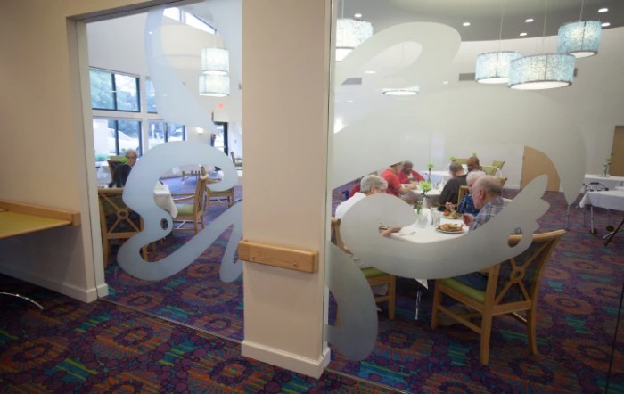 A cozy restaurant interior with people dining at tables, featuring patterned carpets and frosted glass decor.