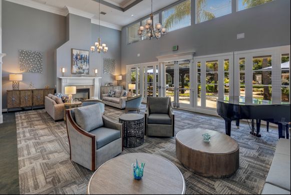 A spacious and elegantly designed living room featuring comfortable seating, a grand piano, and large windows that allow natural light to flood the space.