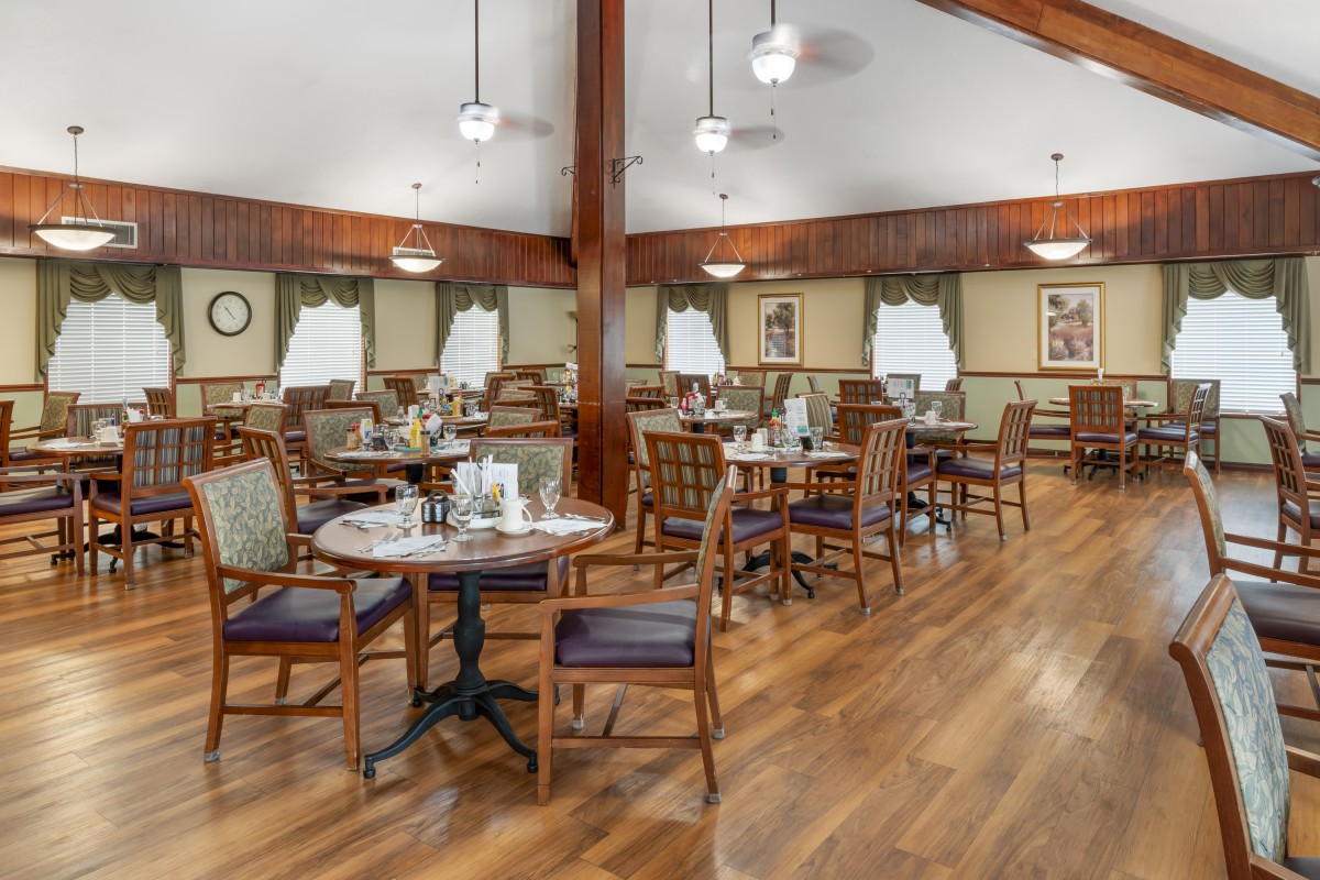 A cozy dining room with neatly arranged tables and chairs, featuring wood flooring and warm lighting.