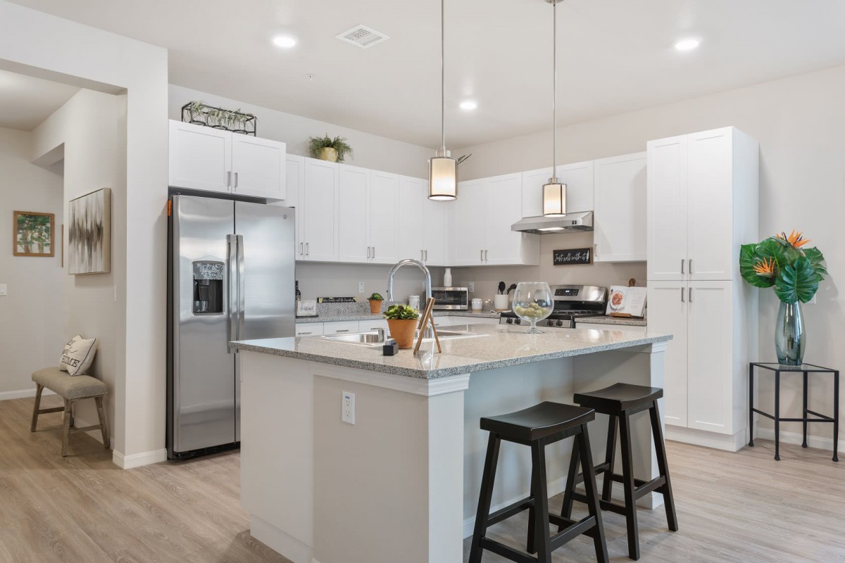 Modern kitchen with white cabinets and a central island featuring pendant lighting and bar stools.