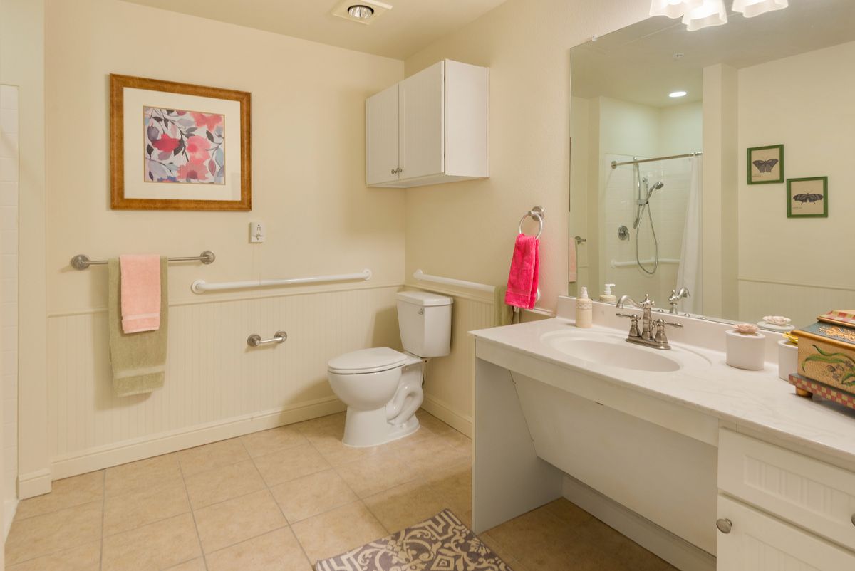 A well-lit bathroom featuring a toilet, sink, mirror, and shower with a red towel for an accent.