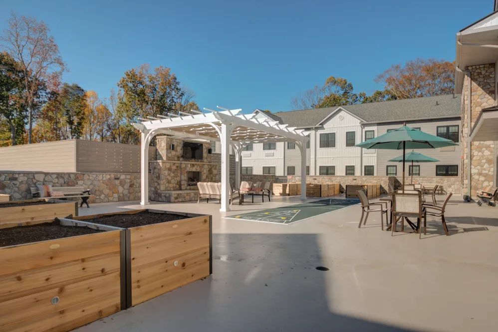 A modern outdoor patio area featuring a pergola, seating, and landscaped surroundings on a sunny day.