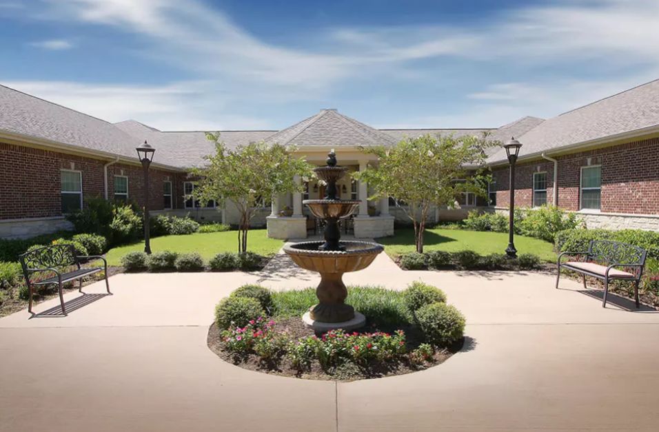 A beautiful courtyard with a central fountain surrounded by lush greenery and a pathway leading to a building.