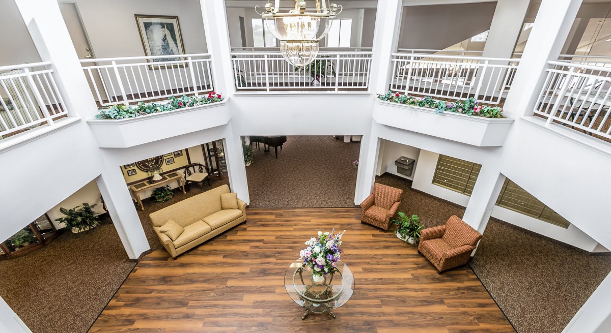 A spacious lobby area with wooden flooring, featuring a central decorative table and comfortable seating arrangements under an elegant chandelier.