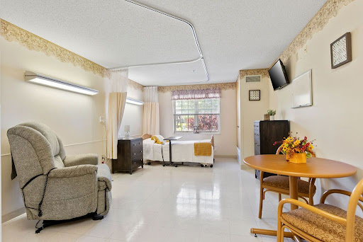 A well-lit hospital room featuring a bed, comfortable chair, and a dining table, designed for patient care.