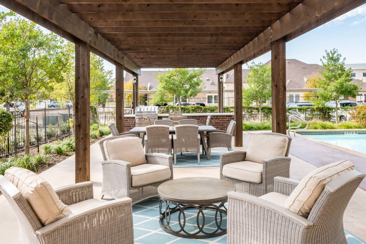 An inviting outdoor seating area under a pergola, featuring wicker chairs and a coffee table with a garden view.