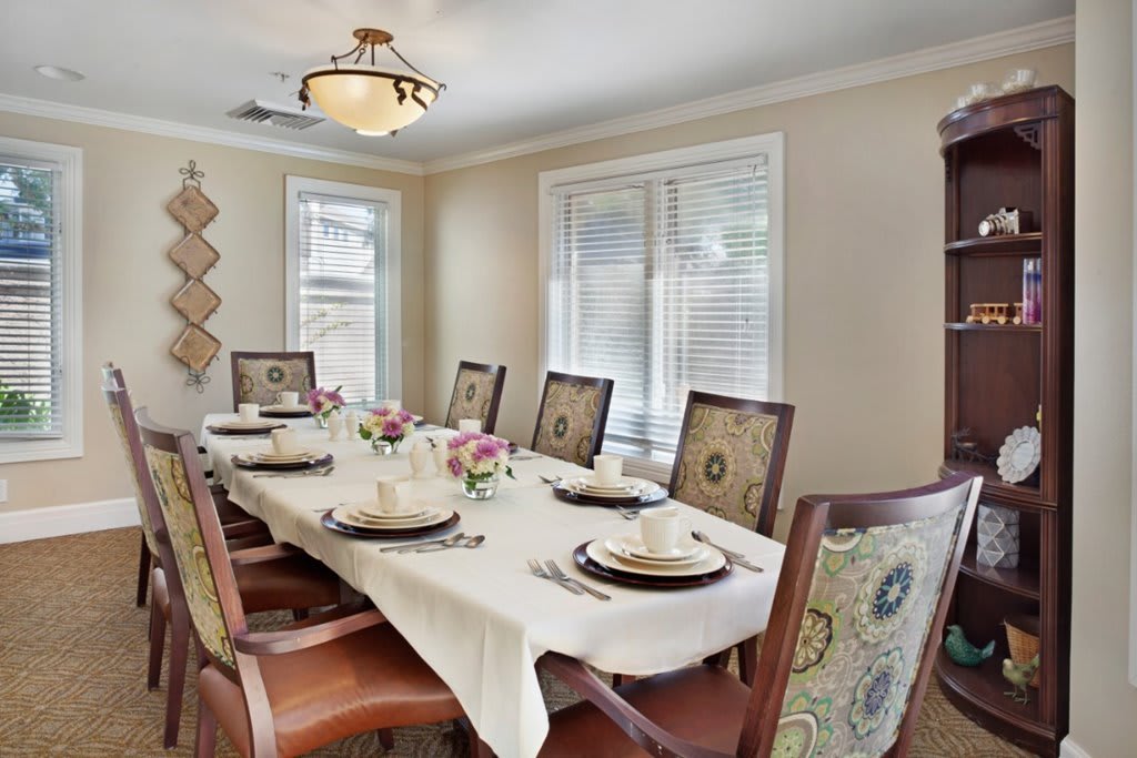 A well-decorated dining room featuring a long table set for a meal with elegant chairs and floral centerpieces.