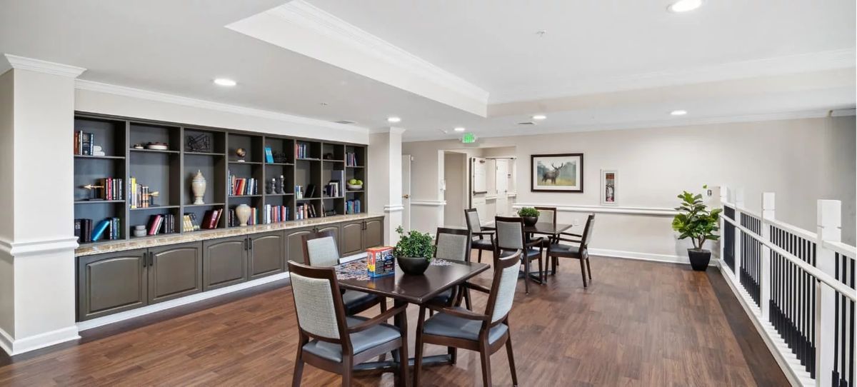 A modern room with tables and chairs, featuring a bookshelf and decorative plants.