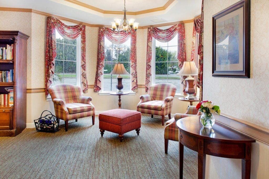A cozy and elegantly decorated living room with traditional armchairs, an ottoman, and large windows adorned with curtains.